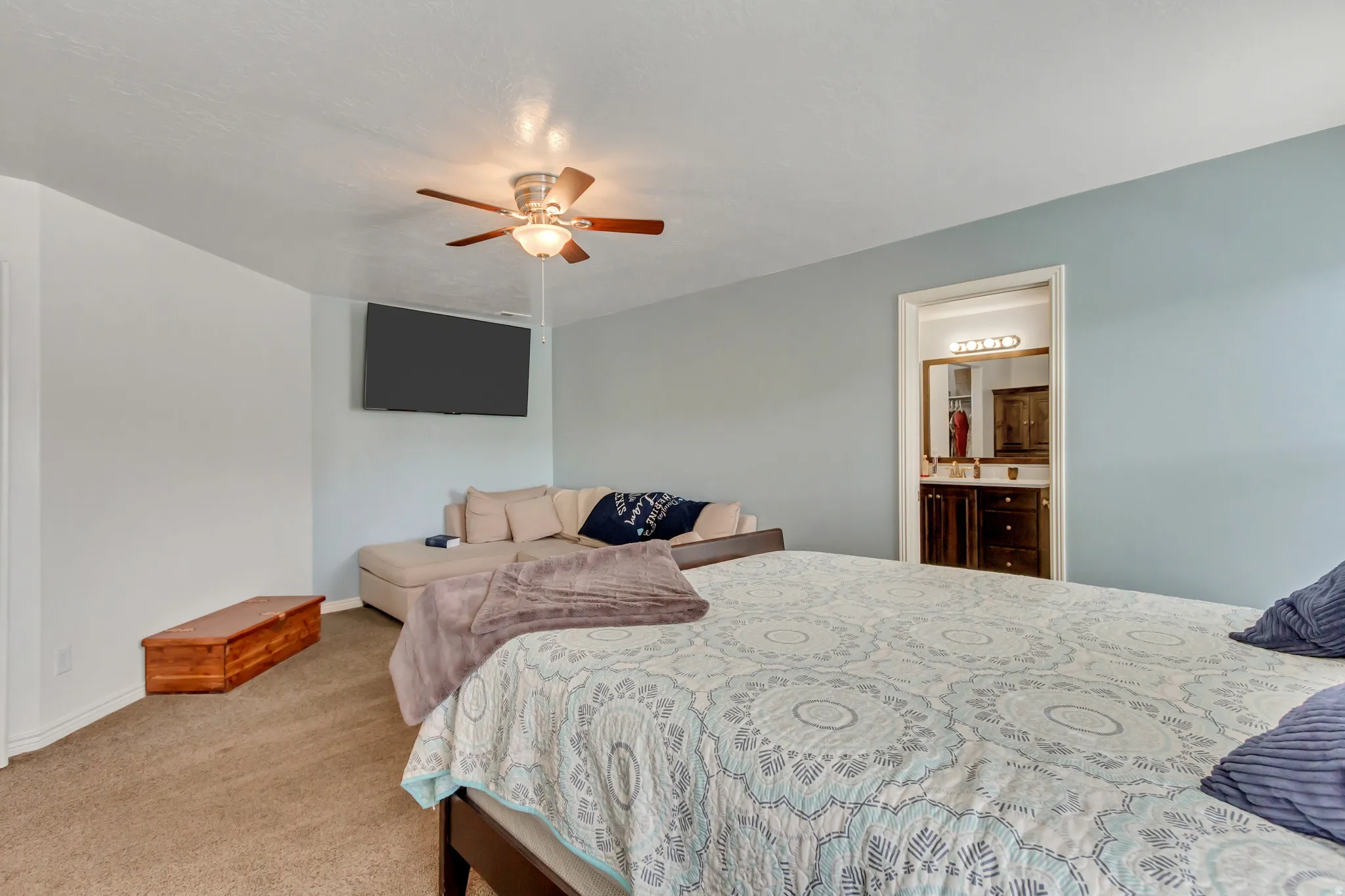 Bedroom featuring light carpet, ensuite bath, and a ceiling fan