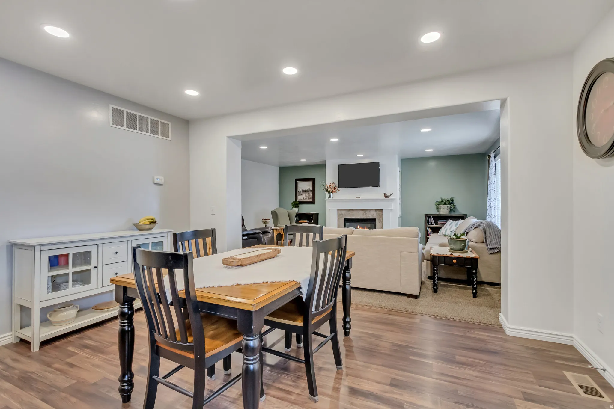 Dining room with wood finished floors, a warm lit fireplace, and recessed lighting