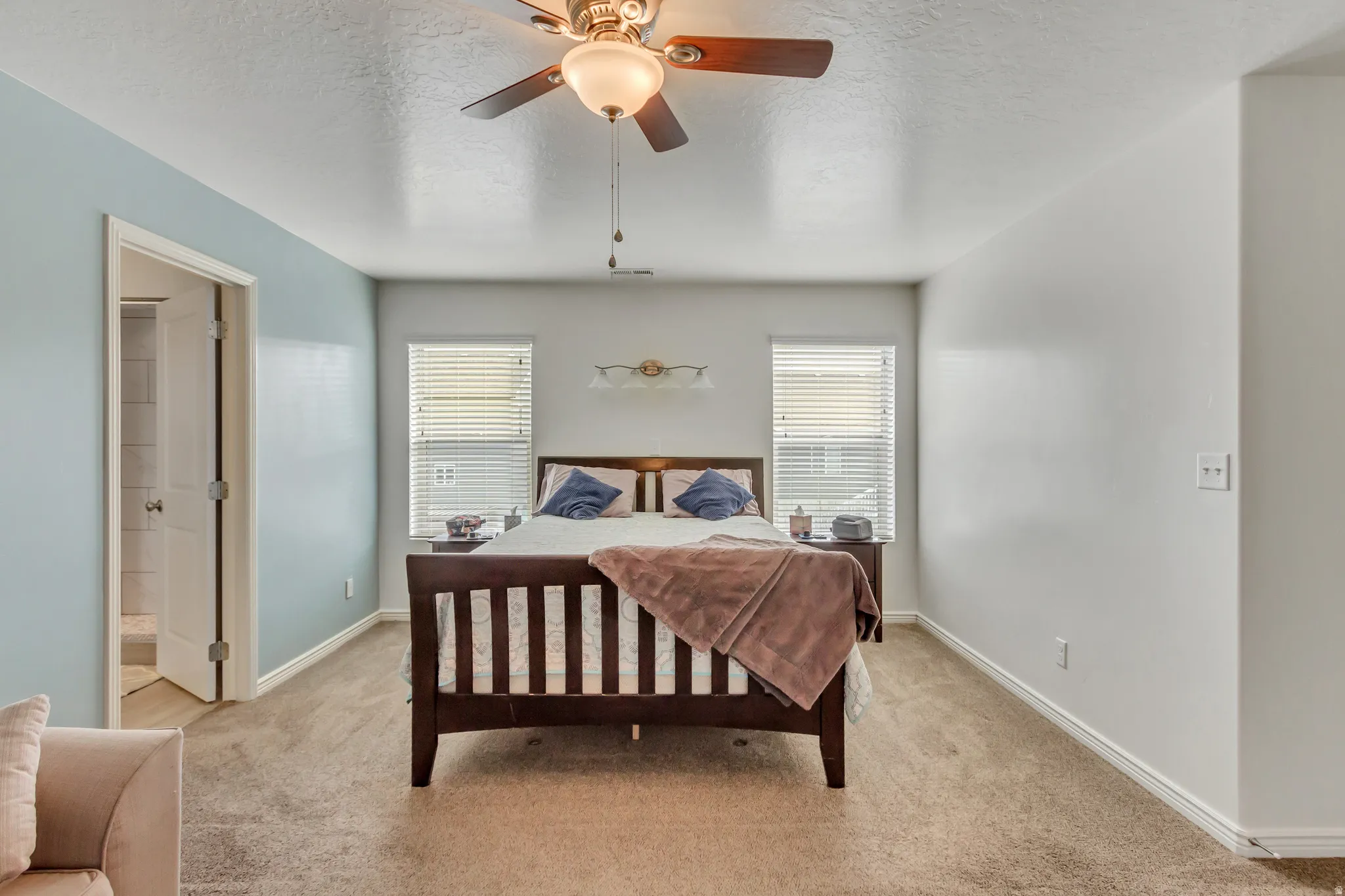 Bedroom featuring a textured ceiling, carpet, multiple windows, a ceiling fan, and connected bathroom