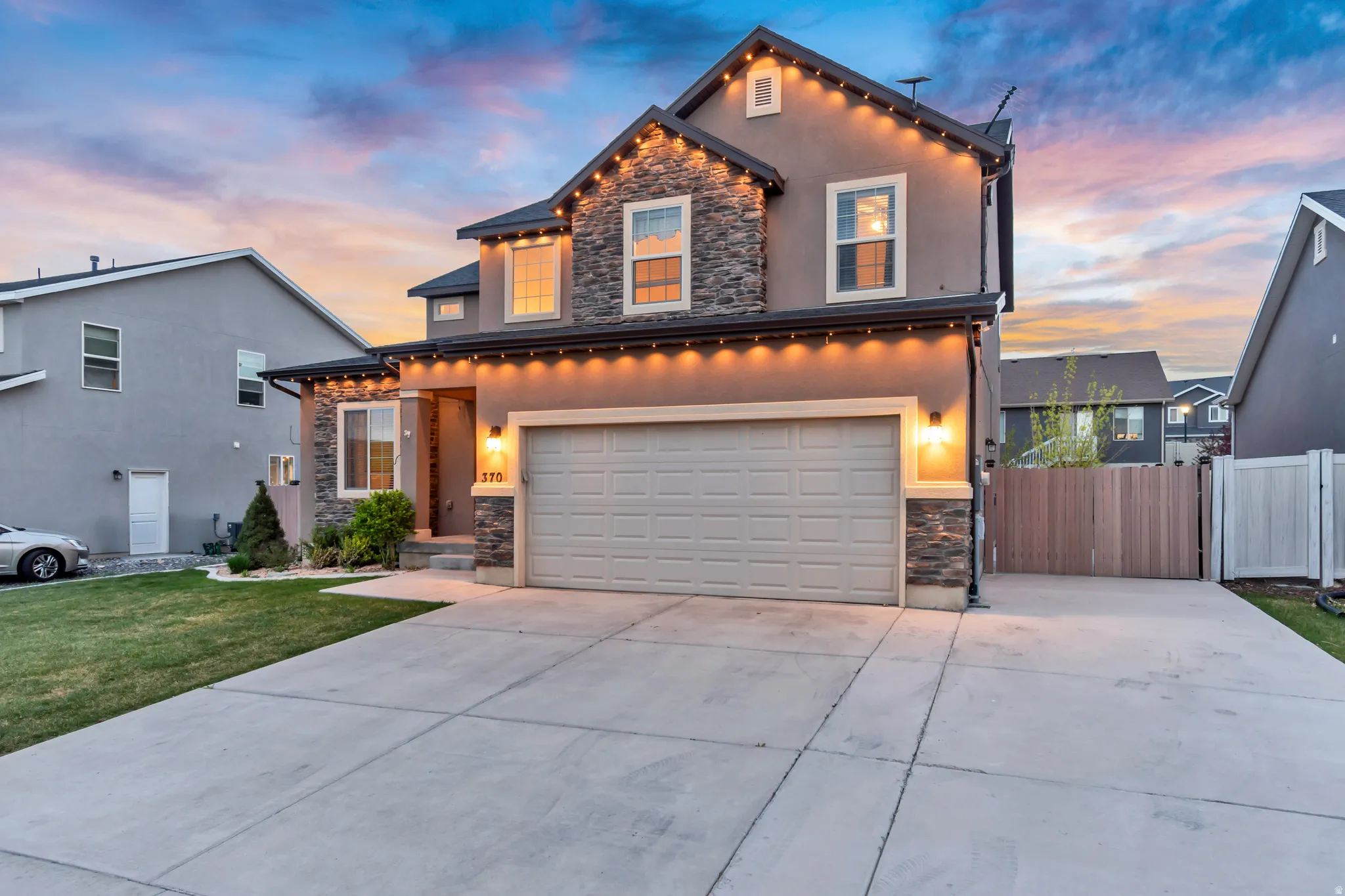 View of front of property with stone siding, driveway, a garage, stucco siding, and a gate