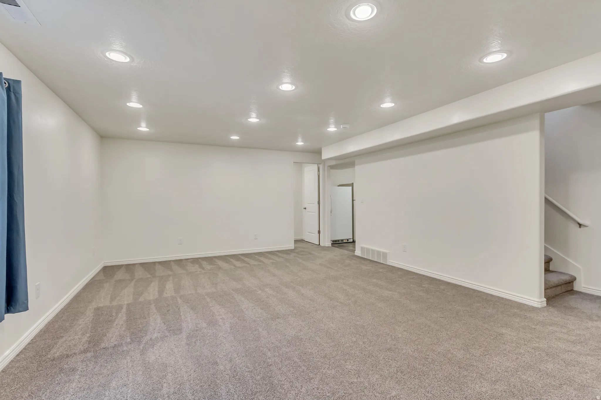 Finished below grade area featuring light colored carpet, recessed lighting, and freestanding refrigerator