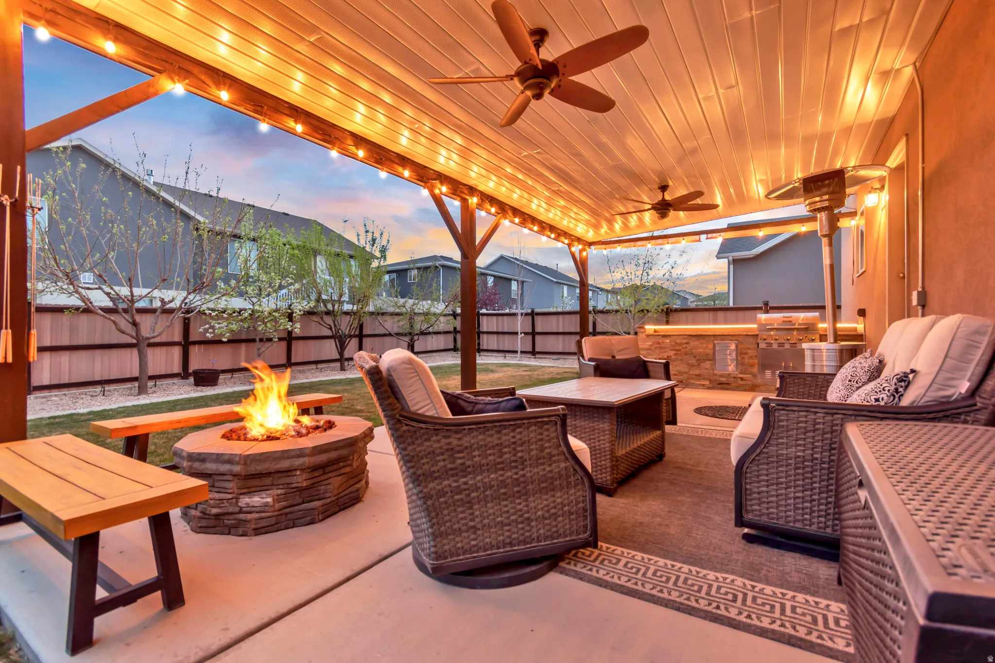 Patio terrace at dusk with a patio, a fire pit, a ceiling fan, a fenced backyard, and an outdoor kitchen and area to lounge