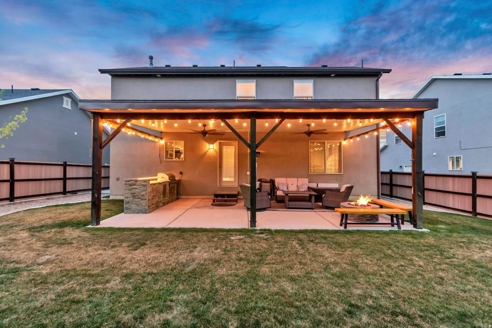 Rear view of house with stucco siding, a patio, a fenced backyard, a fire pit, and an outdoor kitchen and area to lounge