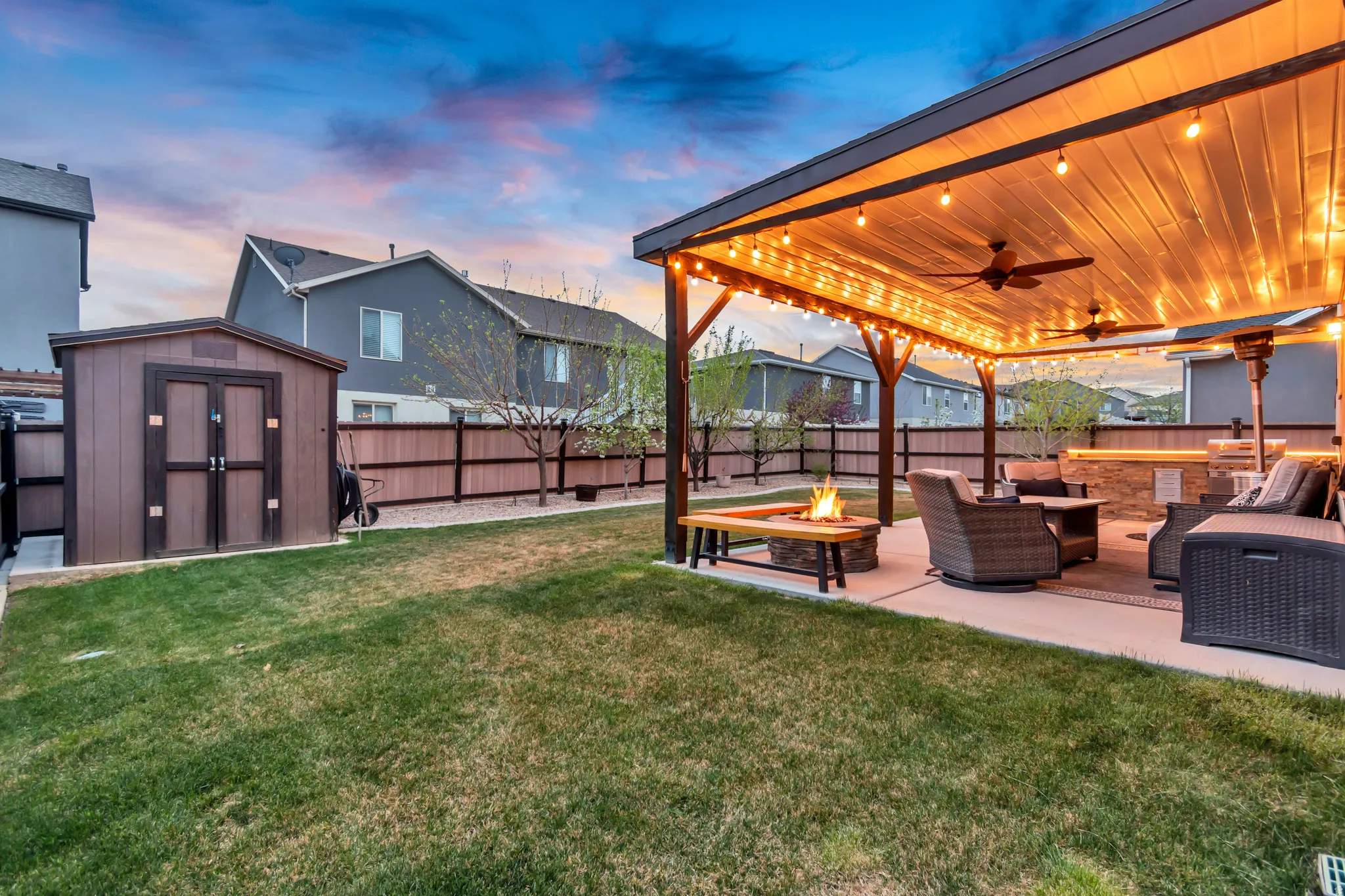 Yard at dusk featuring a ceiling fan, a storage unit, a patio area, and a fenced backyard