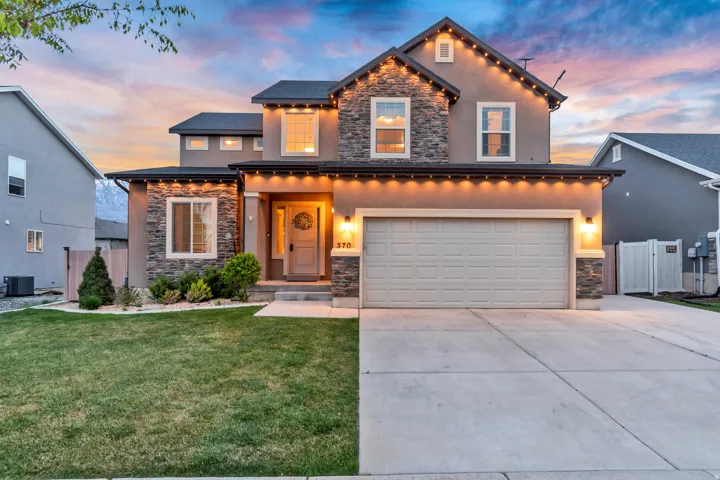 View of front of house featuring stone siding, driveway, stucco siding, and an attached garage