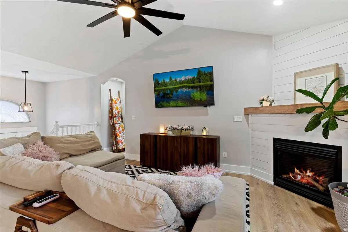 Living area with ceiling fan, wood finished floors, a large fireplace, and arched walkways