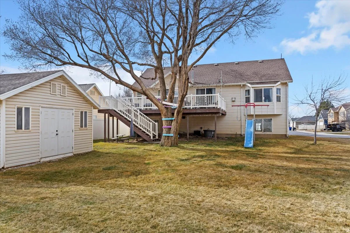 Rear view of property featuring an outdoor structure, a lawn, a wooden deck, and roof with shingles