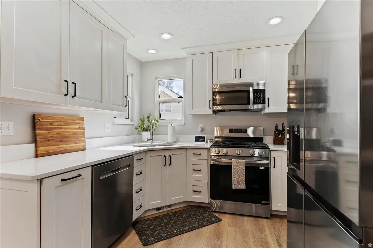 Kitchen with stainless steel appliances, white cabinetry, recessed lighting, light wood-style flooring, and light stone countertops