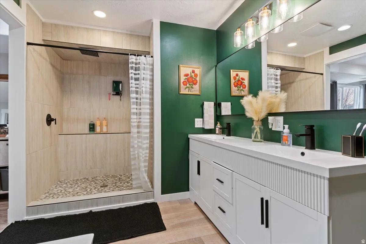 Full bath with double vanity, a tile shower, light wood-type flooring, and recessed lighting