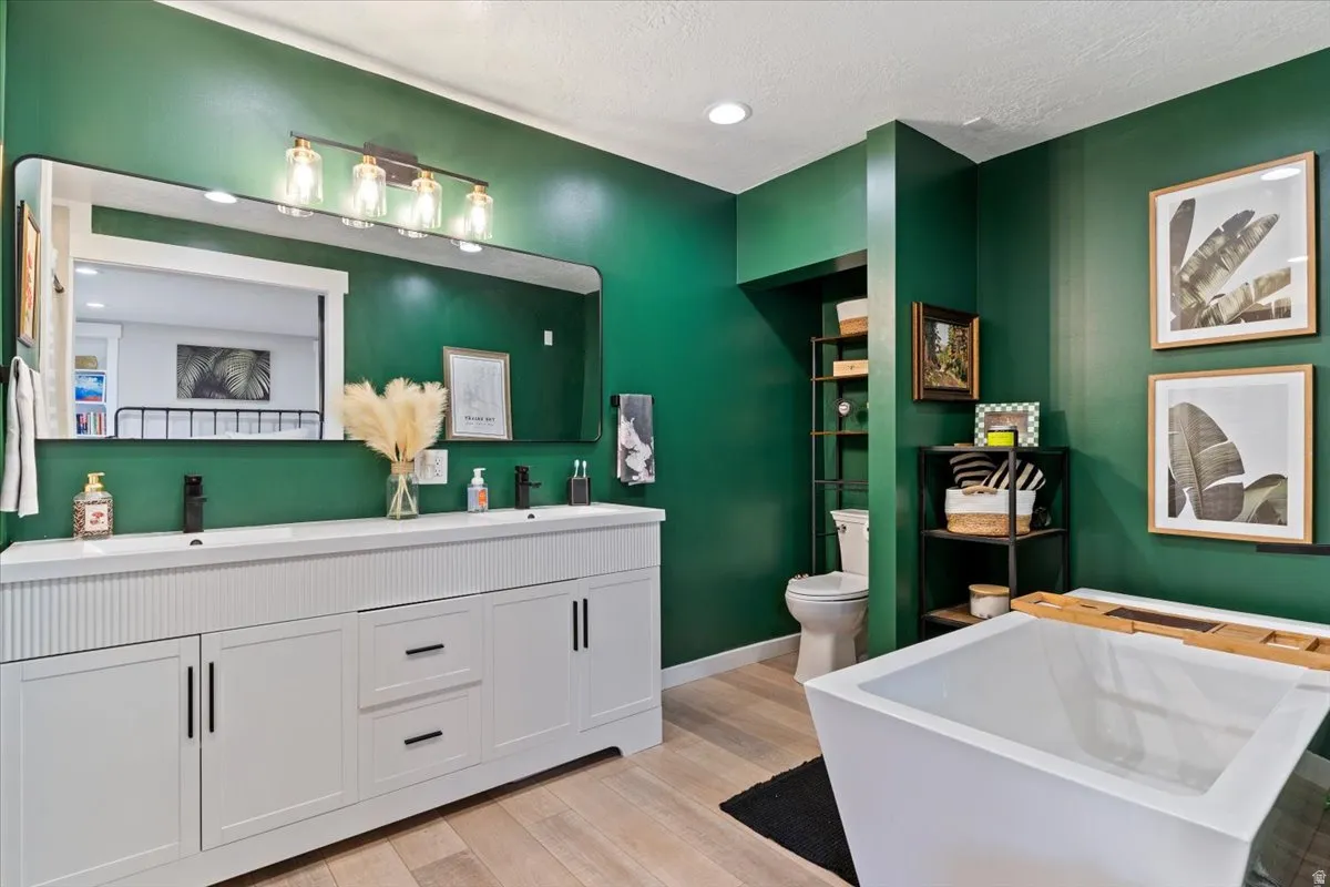 Full bathroom with double vanity, light wood-style flooring, a freestanding bath, recessed lighting, and a textured ceiling