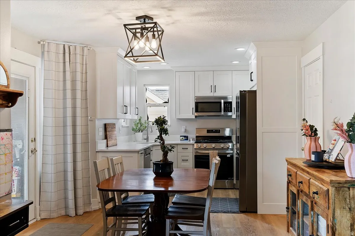 Kitchen featuring stainless steel appliances, a textured ceiling, light wood finished floors, white cabinets, and pendant lighting