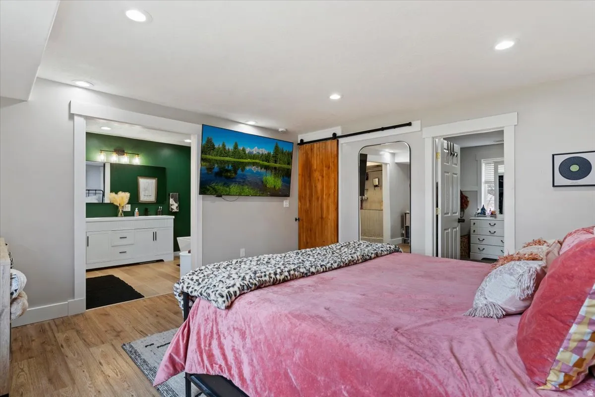 Bedroom featuring ensuite bathroom, light wood-type flooring, a barn door, and recessed lighting