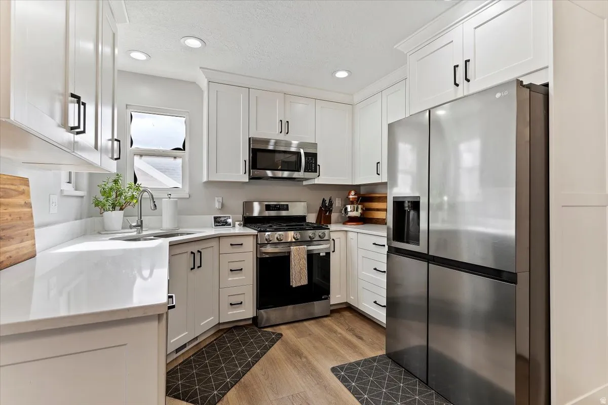 Kitchen with stainless steel appliances, white cabinetry, light wood finished floors, recessed lighting, and light stone counters