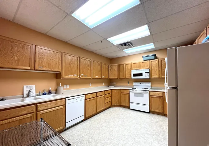 community Kitchen featuring white appliances, a drop ceiling, light countertops, light flooring, and wood finish cabinetry