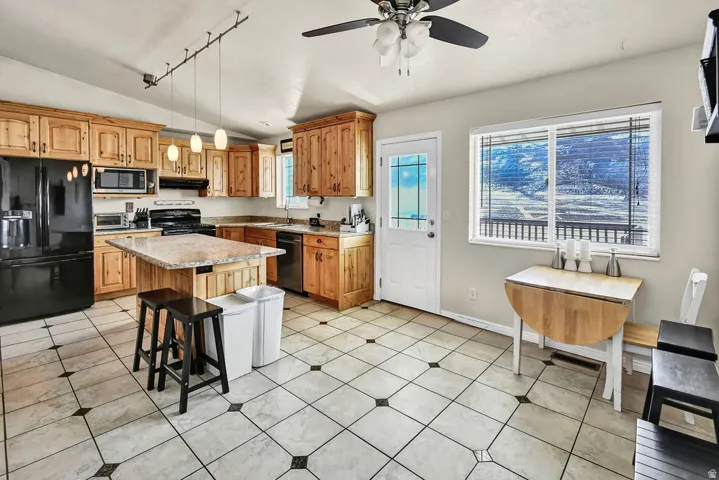 Kitchen with black appliances, a breakfast bar area, light stone countertops, a kitchen island, and rail lighting
