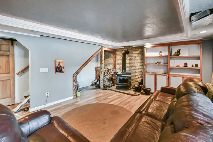 Living room featuring wood finished floors, a wood stove, crown molding, recessed lighting, and a tray ceiling