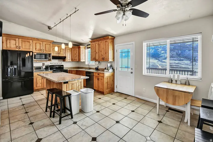 Kitchen featuring black appliances, a breakfast bar, a ceiling fan, a center island, and track lighting