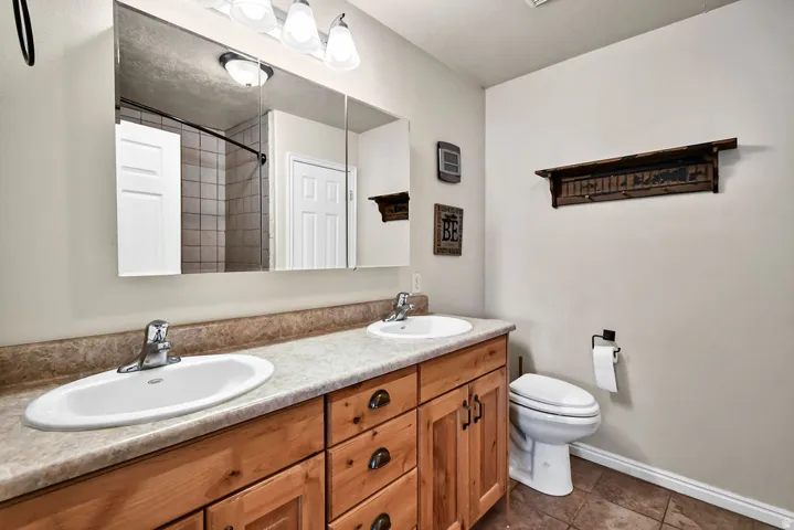 Full bath featuring double vanity, dark tile patterned floors, and a shower