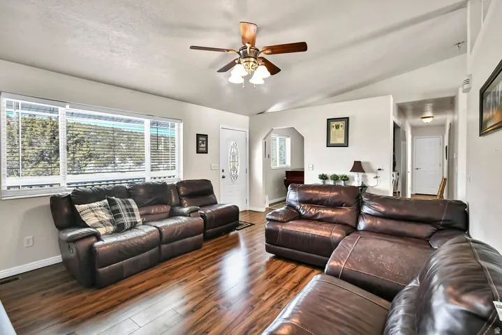 Living room featuring vaulted ceiling, wood finished floors, ceiling fan, plenty of natural light, and arched walkways