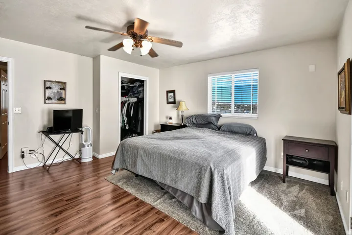 Bedroom with a walk in closet, ceiling fan, a textured ceiling, and dark wood finished floors