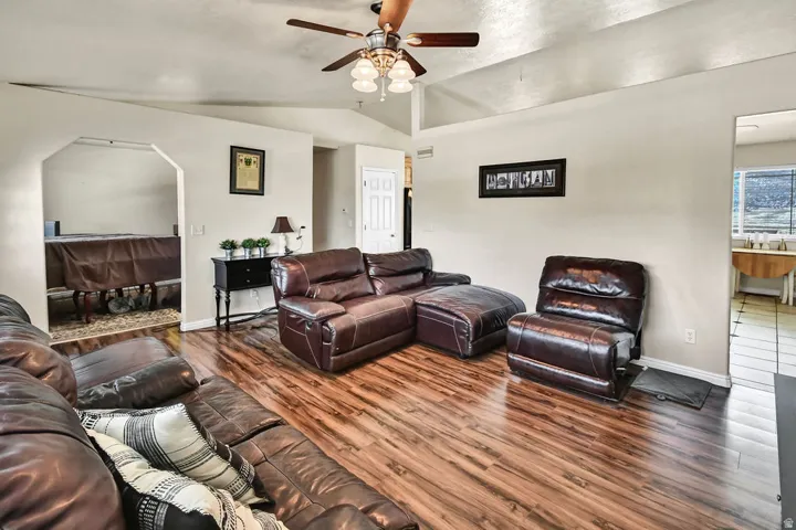 Living room with vaulted ceiling, wood finished floors, ceiling fan, and arched walkways