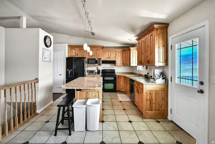Kitchen featuring stainless steel appliances, vaulted ceiling, a kitchen island, a breakfast bar area, and decorative light fixtures