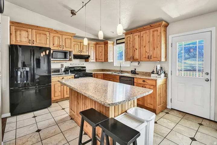 Kitchen with black appliances, a center island, decorative light fixtures, light stone countertops, and vaulted ceiling