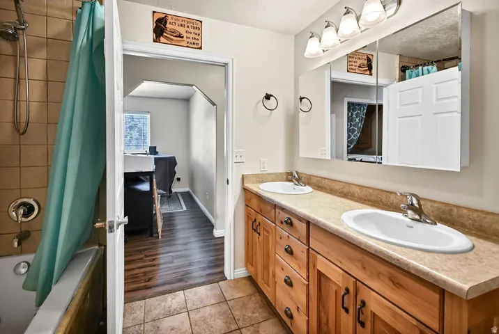 Full bath featuring double vanity, shower / bathtub combination with curtain, and light tile patterned floors