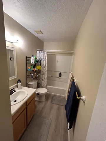 Full bath with vanity, dark wood-type flooring, shower / bath combo with shower curtain, and a textured ceiling