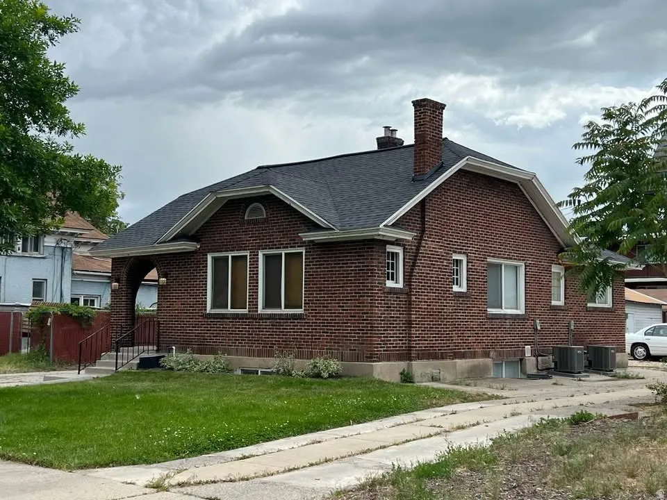 View of side of home featuring brick siding, a yard, a chimney, and a shingled roof