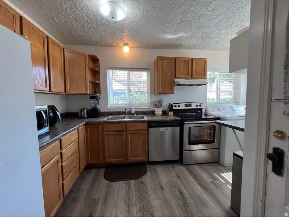 Kitchen with dark countertops, stainless steel appliances, wood finish cabinets, open shelves, and a textured ceiling