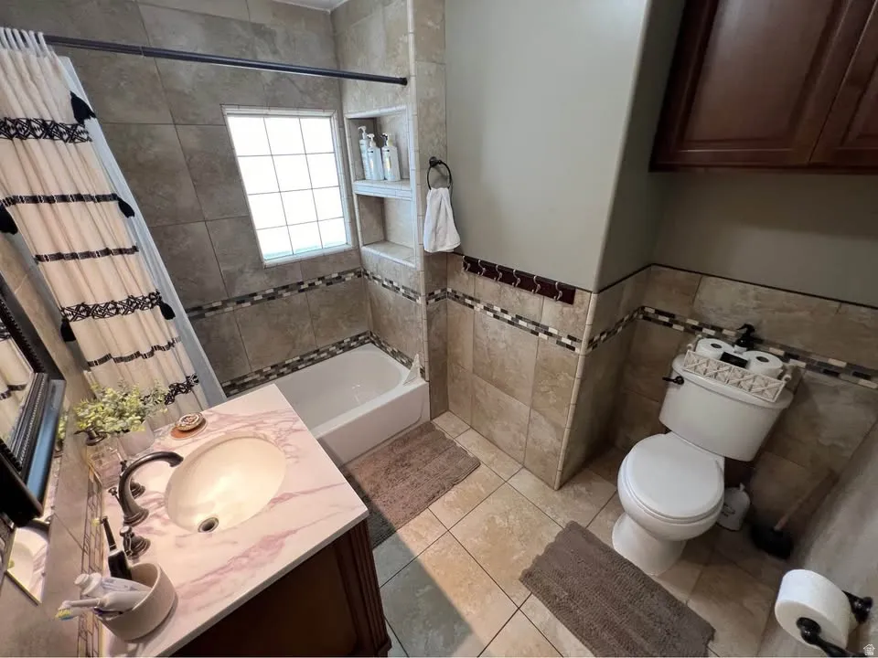 Full bathroom featuring vanity, shower / tub combo with curtain, tile walls, a wainscoted wall, and light tile patterned flooring