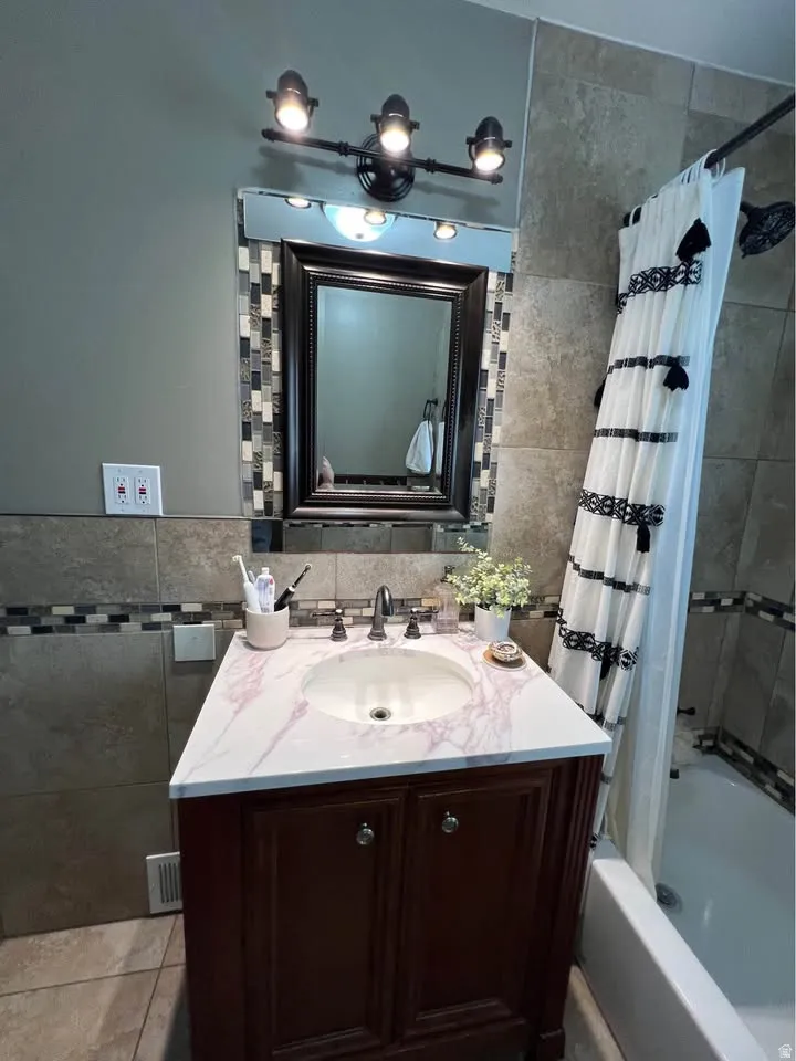 Full bath with tile walls, vanity, and shower / bathtub combination with curtain