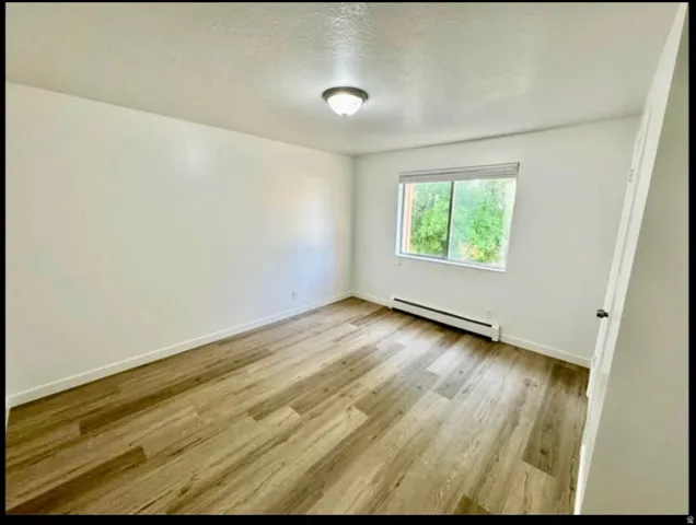 Empty room featuring baseboard heating, light wood-style floors, and a textured ceiling