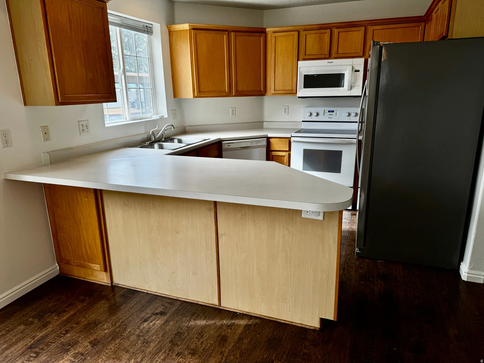 Kitchen featuring stainless steel appliances, a peninsula, light countertops, wood finish cabinetry, and dark wood finished floors