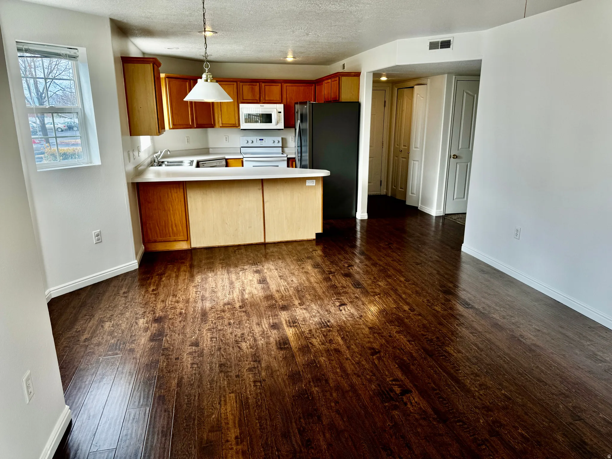 Kitchen with a peninsula, wood finish cabinets, light countertops, white appliances, and a textured ceiling