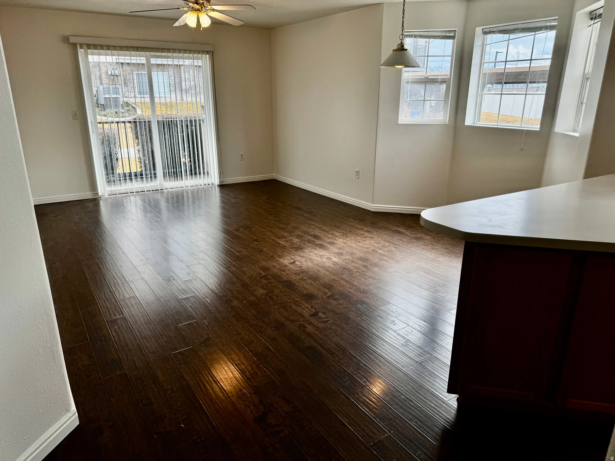 Unfurnished living room with healthy amount of natural light, ceiling fan, and dark wood-type flooring