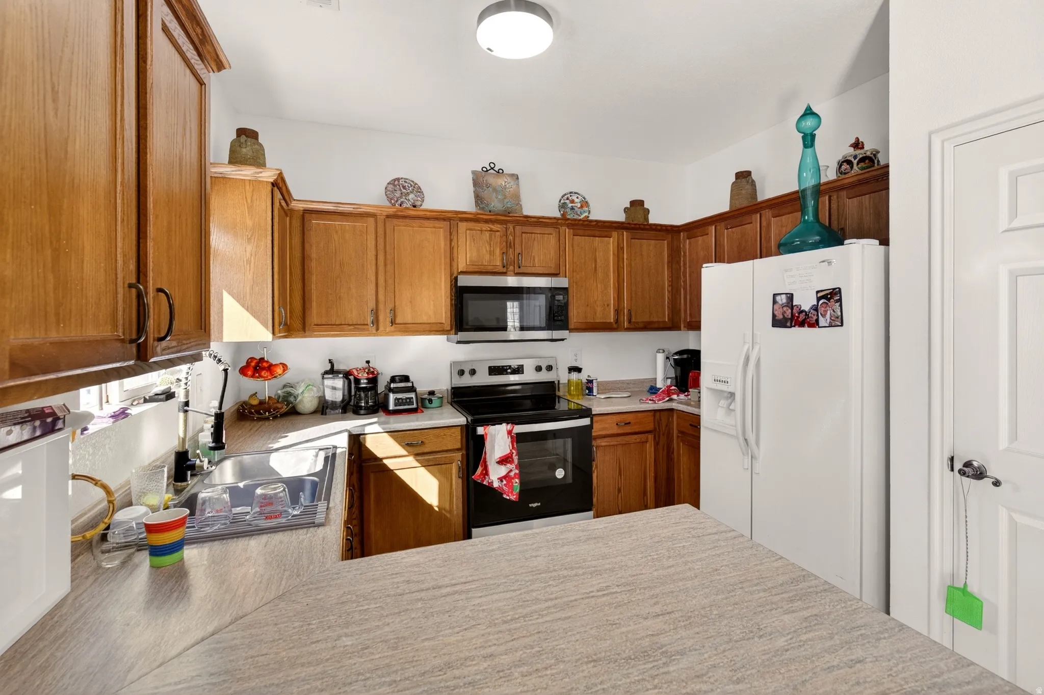 Kitchen with electric range oven, white fridge with ice dispenser, stainless steel microwave, and light countertops