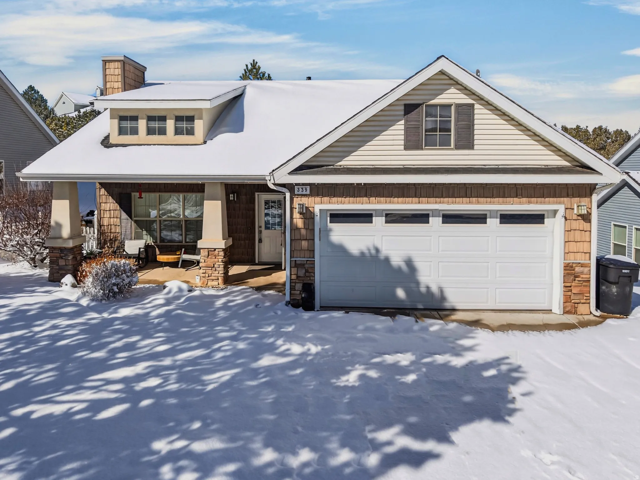 View of front of home featuring stone siding, a garage, covered porch, and a chimney