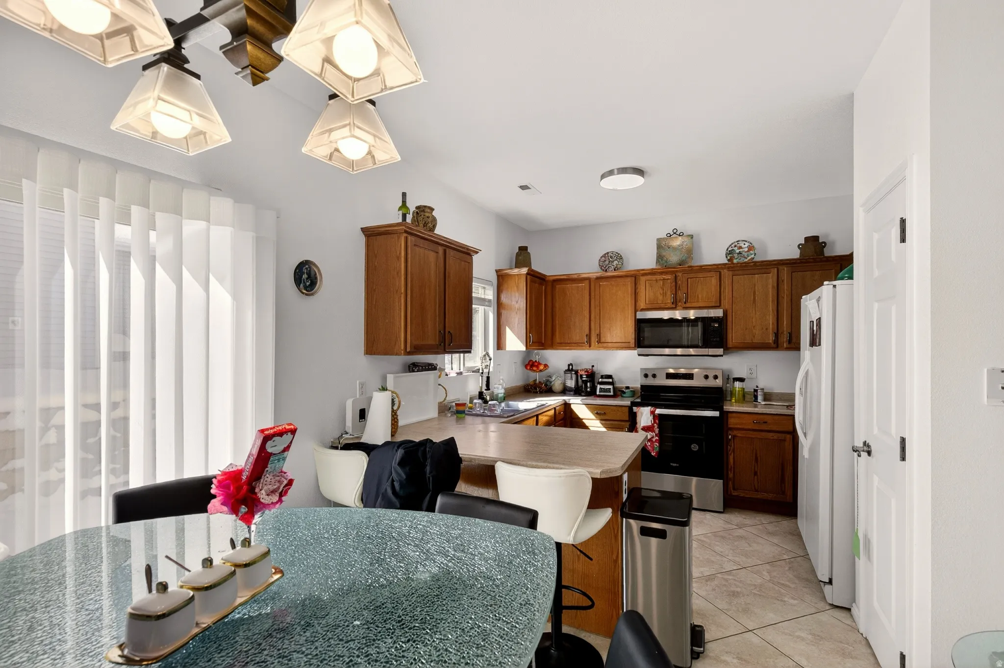 Kitchen with wood finish cabinets, stainless steel appliances, light countertops, a breakfast bar, and light tile patterned flooring