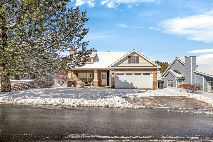 View of front facade featuring a chimney, stone siding, covered porch, and driveway
