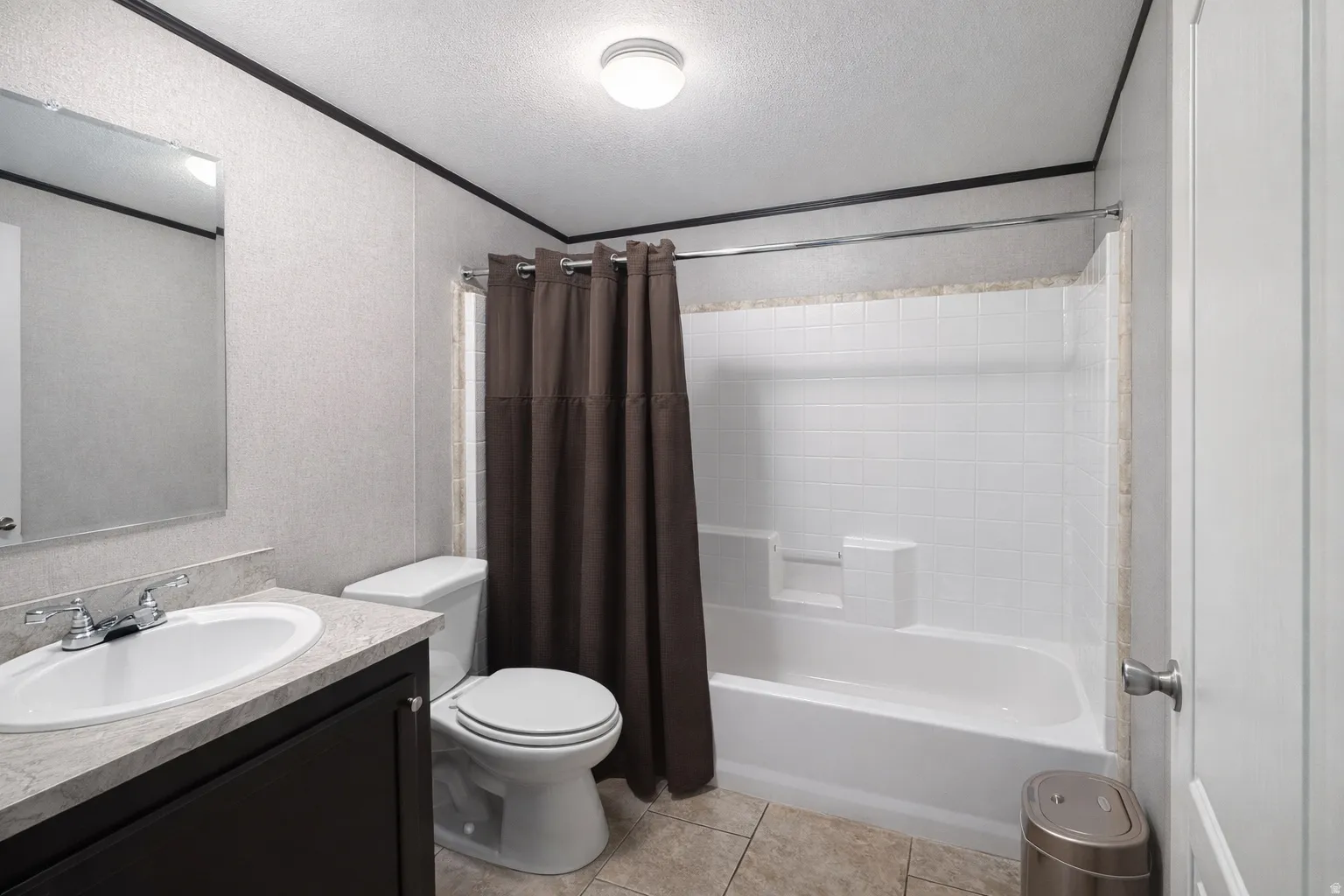 Full bathroom featuring vanity, shower / tub combo with curtain, a textured ceiling, light tile patterned flooring, and ornamental molding