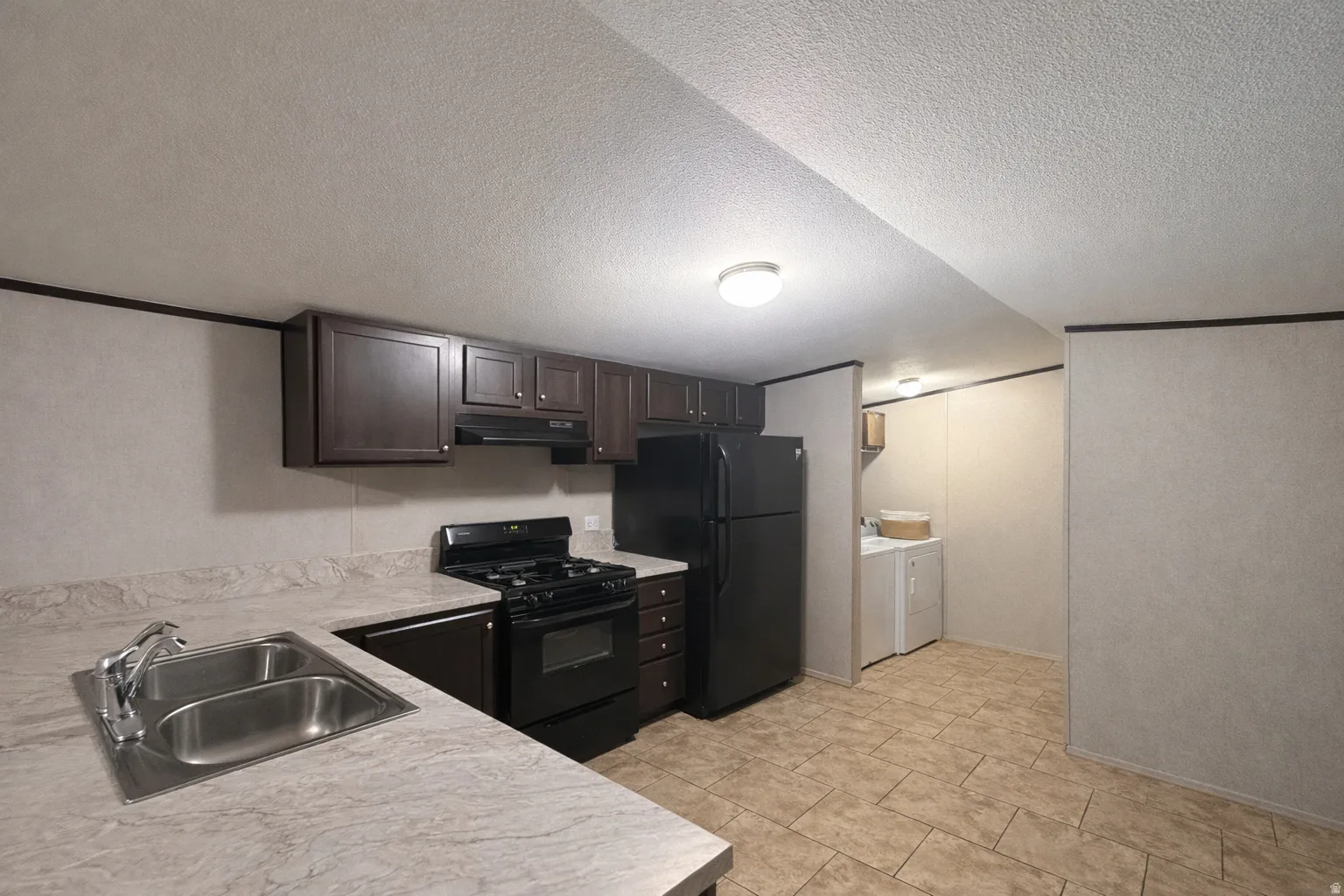 Kitchen with black appliances, light countertops, a textured ceiling, washer and clothes dryer, and dark wood finish cabinetry