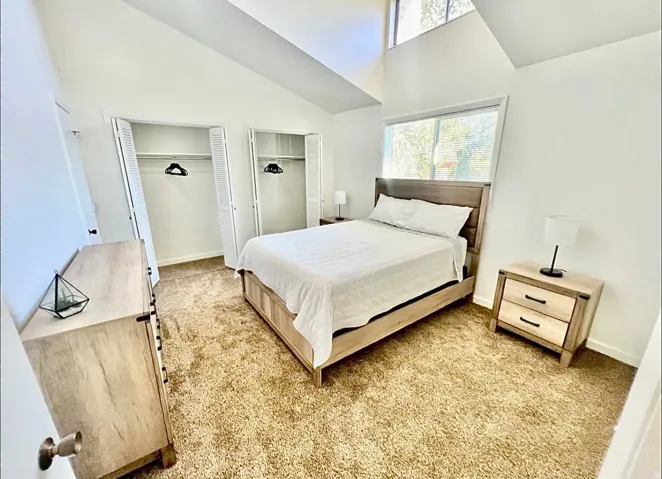 Bedroom with multiple closets, carpet flooring, and vaulted ceiling