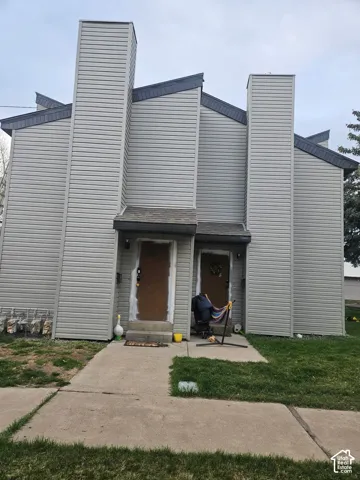 Multi-unit exterior featuring light gray horizontal siding, prominent dual chimneys, asphalt shingle roofing, and concrete entry walkways