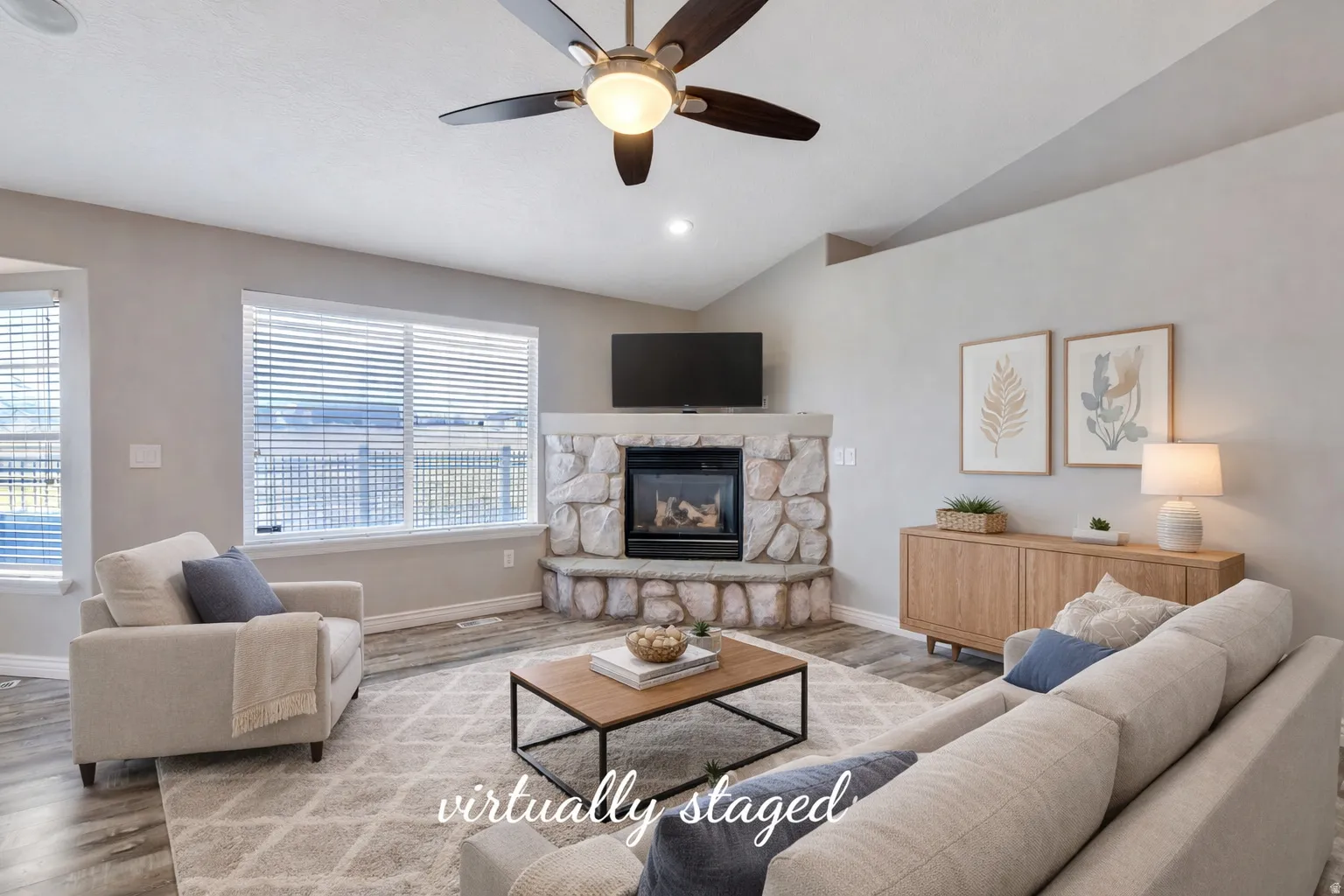 Living area with ceiling fan, wood finished floors, lofted ceiling, and a stone fireplace