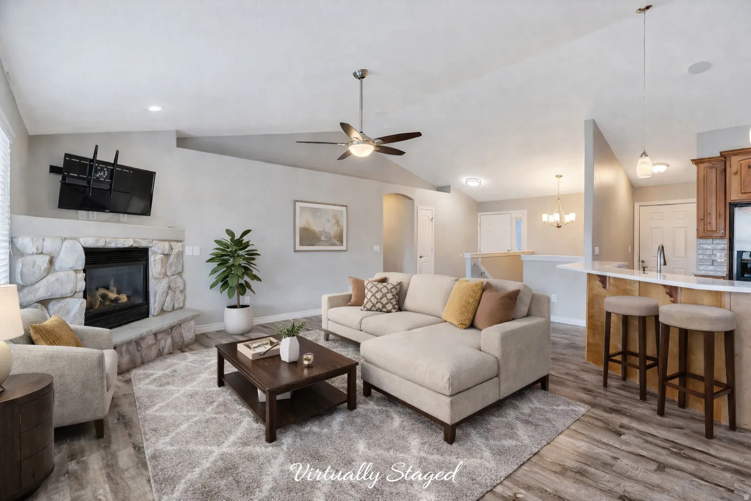 Living area featuring vaulted ceiling, ceiling fan, a stone fireplace, light wood-type flooring, and a chandelier