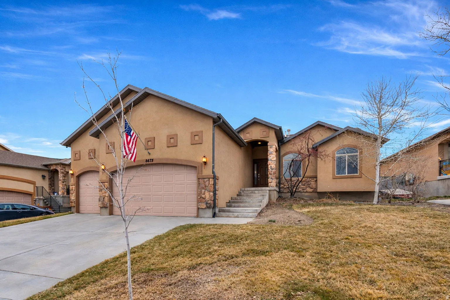 View of front of property featuring an attached garage, stucco siding, driveway, a front lawn, and stone siding
