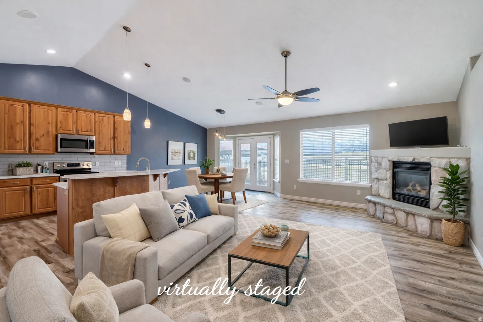 Living area with light wood finished floors, a stone fireplace, and ceiling fan