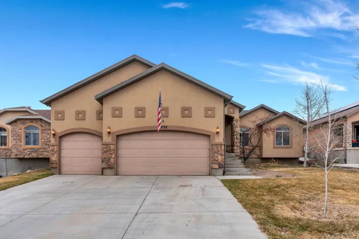View of front of home featuring stucco siding, an attached garage, driveway, and stone siding